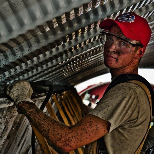 Industrial worker in safety glasses and a cap working inside corrugated metal ducting
