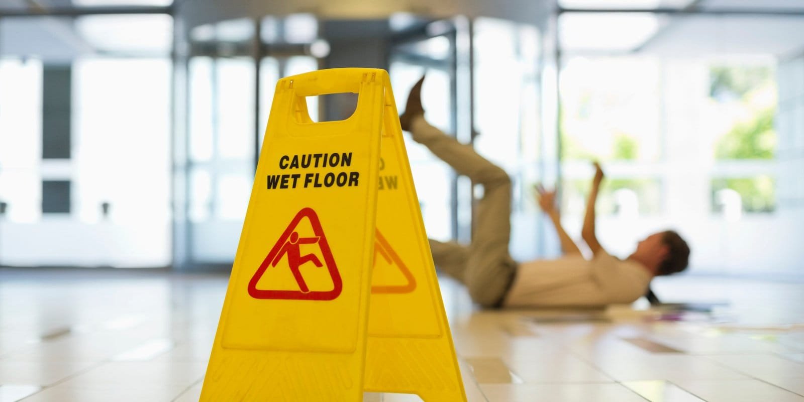 Yellow caution wet floor sign with a worker slipping in the background